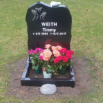 E015 i helpolerad svart granit. Sockel och blomlist, marmorduva på toppen och försänkt vitmålad gravyr.