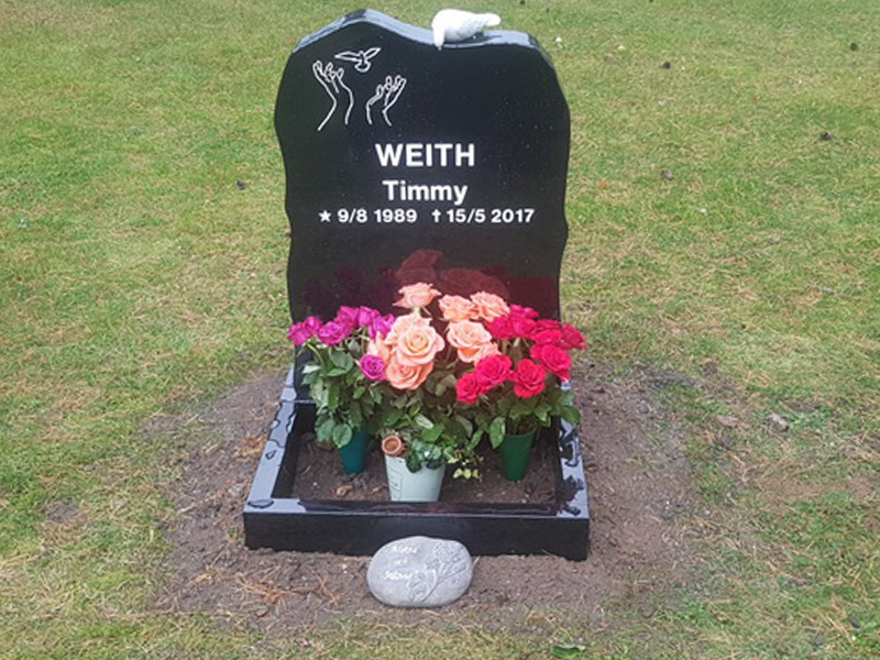 E015 i helpolerad svart granit. Sockel och blomlist, marmorduva på toppen och försänkt vitmålad gravyr.