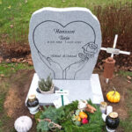 E016 in polished light gray granite with rough-worked side surfaces. All engraving is recessed and painted black. The stone is mounted on a planting base.