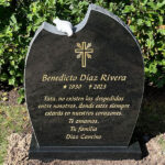 E047 in polished black granite with rough-hewn side surfaces. The engraving is recessed and gilded, with a marble dove at the top.