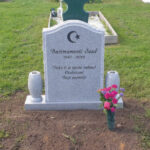 E009 in light gray granite. Polished with rough-hewn edge detailing and side surfaces. Extra-wide base with attached vases; the engraving is recessed and painted black.