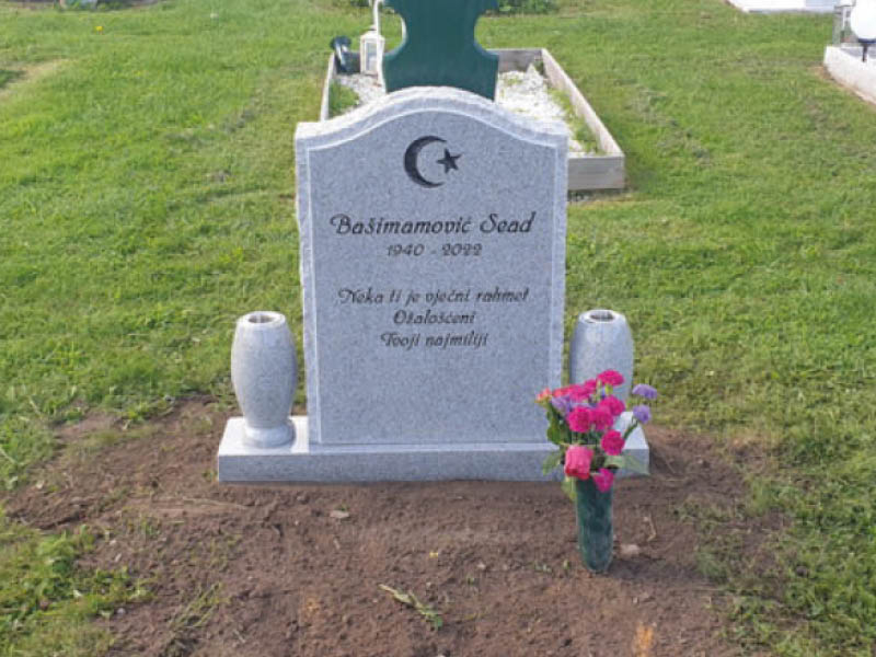 E009 in light gray granite. Polished with rough-hewn edge detailing and side surfaces. Extra-wide base with attached vases; the engraving is recessed and painted black.