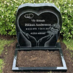 E016 in black granite with a polished flower border. The large decorative motif is recessed and shadow-carved, while the remaining engraving is recessed and painted silver.