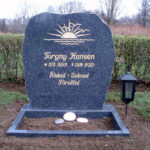 E016 in polished dark gray granite with rough-worked side surfaces. The engraving is recessed and gilded, the flower border is polished, and a marble dove imounted on the top.