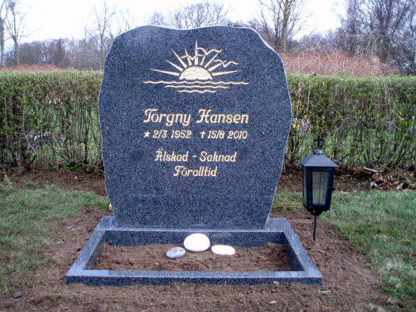 E016 in polished dark gray granite with rough-worked side surfaces. The engraving is recessed and gilded, the flower border is polished, and a marble dove imounted on the top.