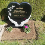 E005 in black granite. Recessed text gilded in gold and recessed decoration painted antique white.