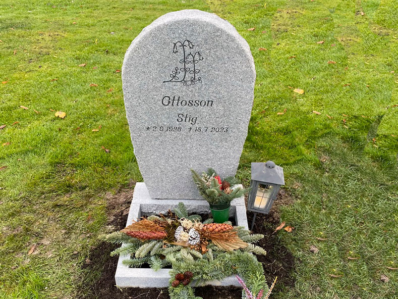 EN117 i flammad grå Kurugranit. Mattslipad blomlist med råarbetade sidytor, gravyr djupblästrad med stenglans.