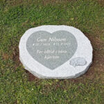 EN114 in fine-polished and fine-chiseled grey Kuru granite. Recessed antique-white text, raised decoration with the inside matte-polished.