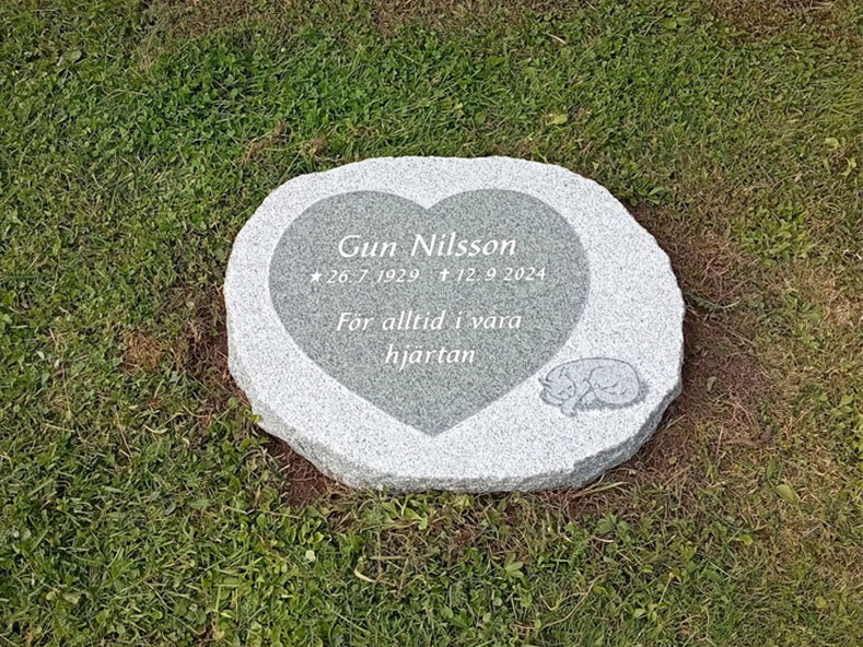 EN114 in fine-polished and fine-chiseled grey Kuru granite. Recessed antique-white text, raised decoration with the inside matte-polished.